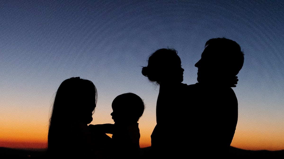 silhouette of 2 women and man standing during sunset